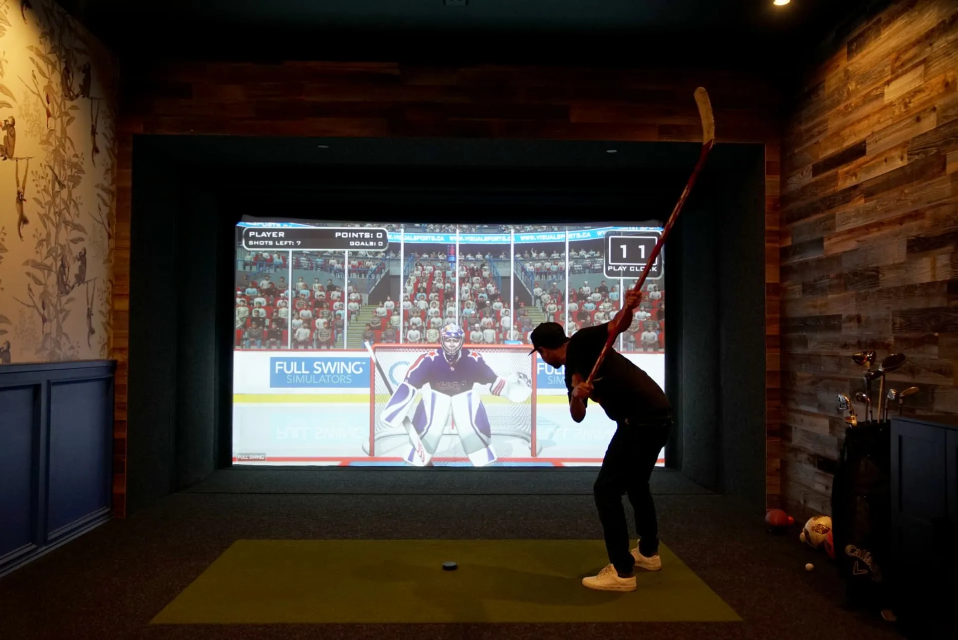 Player winding up for a slap shot at a projected goalie in the Full Swing multi-sport bay