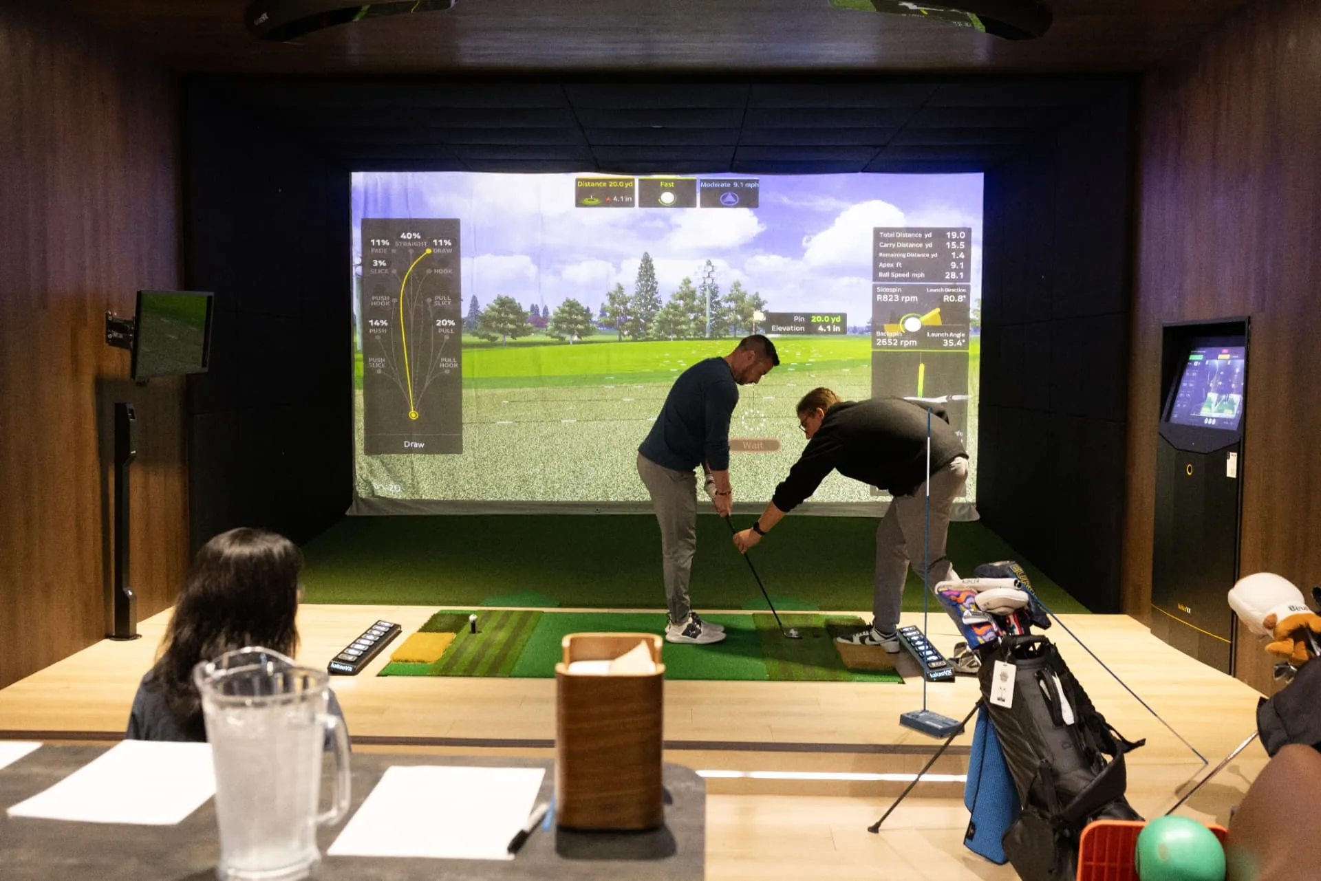 Coach adjusting a golfer's grip during a lesson in a GolfVX simulator bay